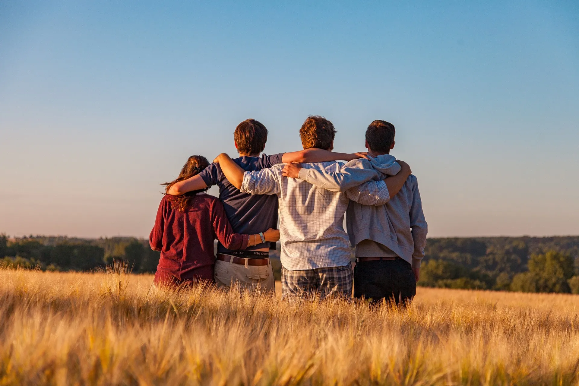 Four friends stand arm in arm in a wheat field, looking into the distance